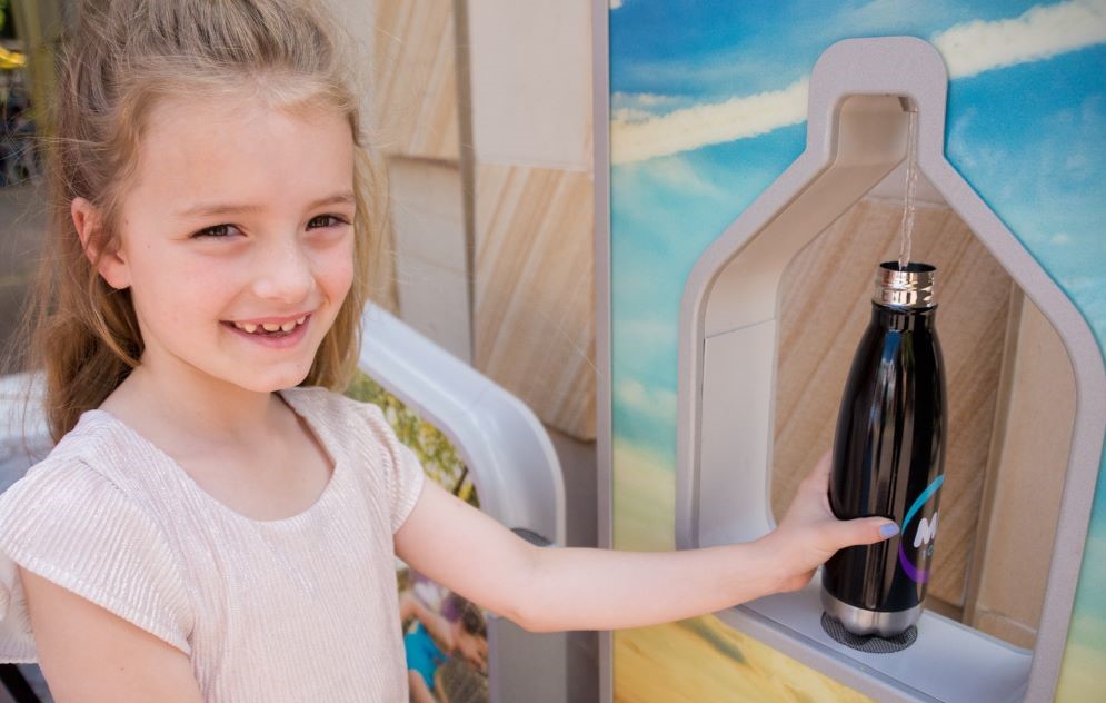 A young girl holding a water bottle next to a water station